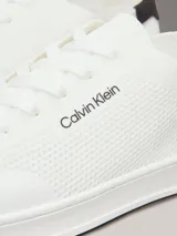 Zapatillas de perfil bajo Calvin Klein confeccionadas en tejido de punto transpirable color blanco. Presentan un diseño minimalista con puntera revestida, suela de goma blanca y detalle de trabilla trasera en piel color negro con el logo de la marca en el lateral y la mediasuela.