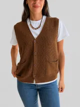 Chaleco tejido de punto color chocolate, con escote en V, cierre frontal de botones y dos bolsillos delanteros. Presenta un diseño de textura cuadriculada en el cuerpo y borde acanalado en la cintura.
