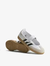 Zapatillas Adidas modelo Samba Jane, con diseño tipo Mary Jane. Presentan una capellada de cuero blanco con las icónicas tres tiras laterales en negro, puntera de gamuza en tono beige y suela de goma tipo gum. Incluyen una tira con cierre de velcro en el empeine.
