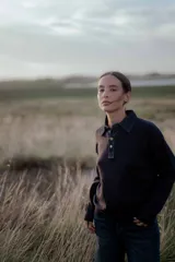 Buzo de punto color azul marino con cuello tipo polo en tela de jean y cierre frontal con botones metálicos. Presenta puños y ruedo acanalados.