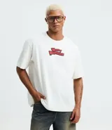 Remera boxy de algodón color blanco, con cuello redondo y mangas cortas. Presenta un estampado grande en la espalda del personaje El Pájaro Loco, con su nombre en rojo y un fondo azul y amarillo, y un globo de diálogo que dice "Guess Who?".
