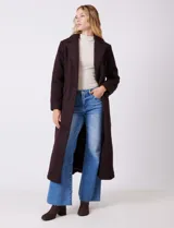 Tapado largo de bouclé color marrón oscuro, con silueta entallada que termina en evasé. Tiene cuello de solapa amplia, cierre frontal con tres botones a tono y bolsillos funcionales con solapa. Incluye forro interno a tono.