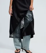 Pollera midi de satén negro con corte evasé, cintura elástica y detalle de entremedio de encaje aplicado en diagonal.
