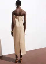 Vestido largo color beige, de diseño recto sin tirantes (palabra de honor) con escote corazón y detalle de pliegues en la parte delantera. Cuenta con cierre de cremallera en la espalda y bolsillos laterales.