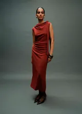 Vestido midi de color terracota, sin mangas, con cuello barco y diseño entallado. Presenta detalles fruncidos en la cintura y un detalle de nudo en el hombro con caída lateral. Incluye forro interior y cierre de cremallera en la parte posterior.
