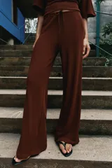 Pantalón palazzo de tiro medio en color marrón, confeccionado en tejido con textura. Cuenta con cintura elástica ajustable mediante cordones y diseño de pierna ancha.