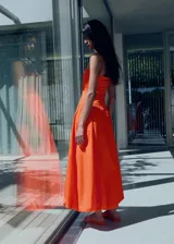 Vestido midi color naranja sin mangas, con escote palabra de honor, tirantes finos marrones y falda estilo globo con bajo abullonado.