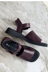 Sandalias de cuero color bordó, con suela plana y gruesa de goma negra, tira ancha en el empeine y tira ajustable con hebilla en el talón.
