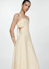 Vestido midi de algodón color crema con diseño bordado tipo broderie. Presenta escote cuadrado, tirantes finos, aberturas laterales cut-out en la cintura y cierre lateral de cremallera.