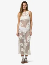 Vestido largo sin mangas confeccionado en encaje color crudo con diseño floral repetido en toda la superficie. Escote redondo y calce estándar. Prenda semi transparente.