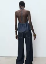 Top de estilo vaquero con escote en pico y espalda descubierta. Presenta un diseño evasé con fruncido elástico en la cintura y cierre mediante lazos en el cuello y el frente.