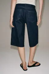 Bermuda de denim azul oscuro de tiro medio y corte recto, perteneciente a la ZARA Woman Collection. Cuenta con diseño de cinco bolsillos, trabillas para cinto y cierre frontal con cremallera y botón metálico.