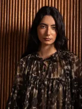 Blusa de gasa con estampado abstracto en tonos oscuros, cuello redondo con lazo ajustable, corte holgado con frunces y mangas largas abullonadas con puños elásticos.