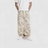Pantalón de jean con corte baggy y diseño de estampado camuflado tipo nieve en tonos beige y gris. Presenta un ajuste holgado, tiro medio y cierre frontal con botón y cremallera.