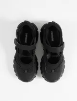 Zapatillas negras de estilo híbrido entre ballerina y champión, con suela robusta tipo track, cierre de velcro y cordones elásticos decorativos en el empeine.