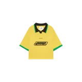 Chomba amarilla de manga corta con cuello polo negro de rib con detalles en verde y puños verdes. Cuenta con estampa gráfica centrada en el pecho y logo de la marca en menor tamaño en la parte superior.