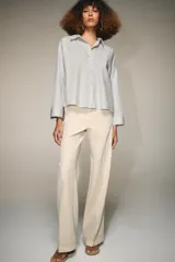 Camisa de popelín color blanco, con cuello solapa, escote en pico y cierre frontal con botones. Presenta un corte holgado y mangas largas con puños rectos.