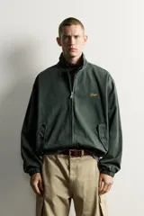 Cazadora relaxed fit de denim de algodón color verde oscuro, con cuello subido y cierre de cremallera frontal. Cuenta con bolsillos de vivo con solapa en la cadera, acabados elásticos y detalle bordado a contraste en el pecho.