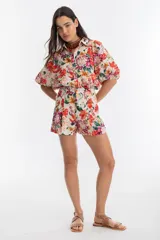 Short de lino color blanco con estampado floral en tonos rojos, amarillos, verdes y rosas. Tiene cintura alta con tablas, bolsillos laterales y cierre frontal con gancho metálico.