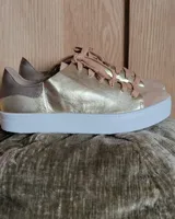 Zapatillas plateadas de cuero con cordones grises y suela blanca.