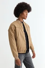 Campera tipo bomber color tostado, con cierre frontal, cuello, puños y ruedo de tejido elástico acanalado. Presenta costuras horizontales en la parte superior del pecho.