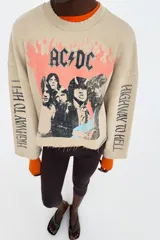 Sudadera beige de mezcla de algodón, con cuello redondo, manga larga y bajo deshilachado. Presenta un estampado frontal de la banda AC/DC con llamas naranjas y el texto "Highway to Hell" en las mangas.