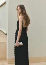 Vestido largo negro de corte recto, con escote en pico, tirantes finos, espalda abierta y diseño revestido con flecos texturizados.