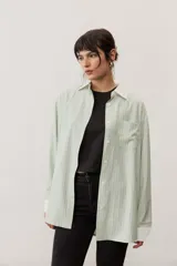 Camisa oversize a rayas color verde menta con cuello y puños en contraste de color blanco. Presenta cierre frontal con botones y un bolsillo aplicado en el pecho.