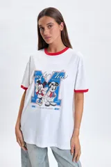 Remera blanca de corte oversize con cuello y bordes de mangas en color rojo. Presenta un estampado frontal con los personajes de Mickey y Minnie Mouse junto a la frase Cool & Chic.