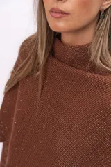 Ruana tejida de punto con cuello alto, confeccionada en una mezcla de algodón y lurex que le otorga un acabado brillante. Presenta un diseño asimétrico con caída fluida y holgada.
