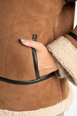 Campera tipo gamulán de corte oversize, confeccionada en material efecto gamuza color camel con interior y detalles de cuello y puños en corderito sintético color crema. Presenta cierre frontal y detalles de ribetes en cuero sintético negro.