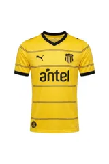 Camiseta de fútbol Puma del Club Atlético Peñarol, modelo Away Jersey Dandelion, color amarillo con finas líneas horizontales negras y detalles en negro en cuello y mangas. Incluye el logo de Puma, el escudo del club y el sponsor Antel en el frente.