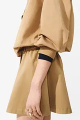 Pollera mini acampanada en sarga de algodón y lyocell, de cintura estándar con cierre, pretina prolongada con botones y elástico revestido en los lados. Cuenta con frunces en la parte superior y bolsillos laterales discretos.