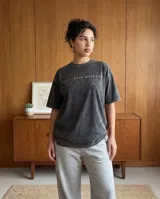 Remera de algodón con efecto stone wash en color negro, de corte oversize y manga corta. Presenta un estampado artístico en la espalda con motivos de figuras estilizadas y hongos en tonos vibrantes.