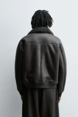 Cazadora oversize de efecto piel color negro, con interior y cuello solapa de pelo sintético gris a contraste. Cuenta con bolsillos de vivo en la cadera, acabados en rib elástico y cierre frontal con cremallera.