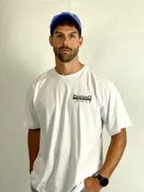 Remera blanca de corte holgado con estampa frontal pequeña en tipografía gótica y texto complementario.