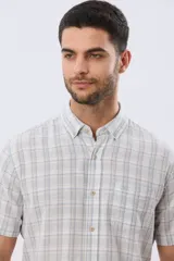 Camisa de manga corta confeccionada en mezcla de lino y algodón, con diseño a cuadros en tonos gris, blanco y azul. Presenta cuello camisero con botones y bolsillo ojal en el pecho con detalle bordado.