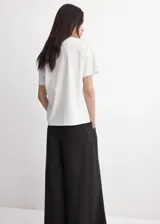 Camiseta blanca de algodón con cuello redondo, mangas cortas y detalle de bordado floral en el frente.