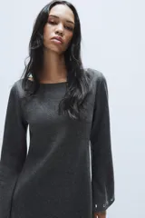 Vestido corto de punto color gris oscuro, con cuello barco y mangas largas acampanadas. Presenta detalles de tachas metálicas aplicadas en el ruedo y en los puños, con un diseño de corte evasé.