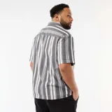 Camisa de manga corta a rayas verticales en tonos negro y blanco, con cuello camisero, cierre frontal de botones y un bolsillo aplicado en el pecho.