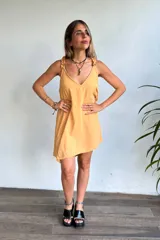 Vestido corto color amarillo mostaza, con escote en V y tirantes finos con detalle de volado o fruncido. El ruedo es asimétrico.