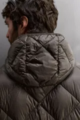 Campera puffer verde oliva acolchada con diseño de rombos, capucha y cierre frontal con cremallera. Incluye bolsillos laterales con cierre. Relleno de plumón y plumas.