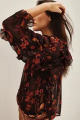 Camisa de viscosa con estampado floral en tonos rojizos y naranjas sobre fondo negro. Presenta volados en los hombros y mangas largas con terminaciones delicadas.