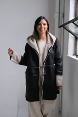 Tapado de cuero sintético negro con interior y detalles en corderito sintético color crema. Presenta capucha, cierre frontal y mangas largas con puños vueltos.