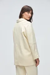 Chaquetón de lana fina sin teñir, con cuello camisero, cierre frontal de botones y bolsillos delanteros. Diseño de corte recto y estructura clásica.