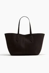 Bolso tipo shopper de color marrón oscuro o negro, con forma curva y dos asas de mano largas. Presenta costura central vertical y detalles de costura en forma de diamante donde se unen las asas al cuerpo del bolso.