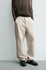 Pantalón relaxed fit color beige, confeccionado en tejido de algodón. Cuenta con bolsillos frontales, bolsillos traseros de plastrón y aplicación de bolsillos plastrón con tira multifunción en la pernera. Cierre frontal con cremallera y botón.