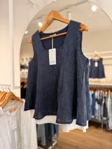 Musculosa azul marino con diseño de doble capa, escote redondo y silueta evasé, que combina una capa superior de textura sutil con una base blanca plisada inferior.