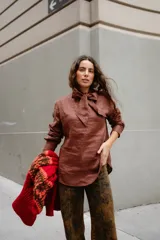 Blusa de lino color marrón con cuello tipo lazo, mangas largas y diseño entallado con pinzas frontales.