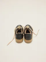 Championes urbanos de cuero negro con diseño trenzado en los laterales y la puntera, cordones en tono tostado y suela de goma. Cuentan con un detalle de aplique metálico dorado en los cordones.